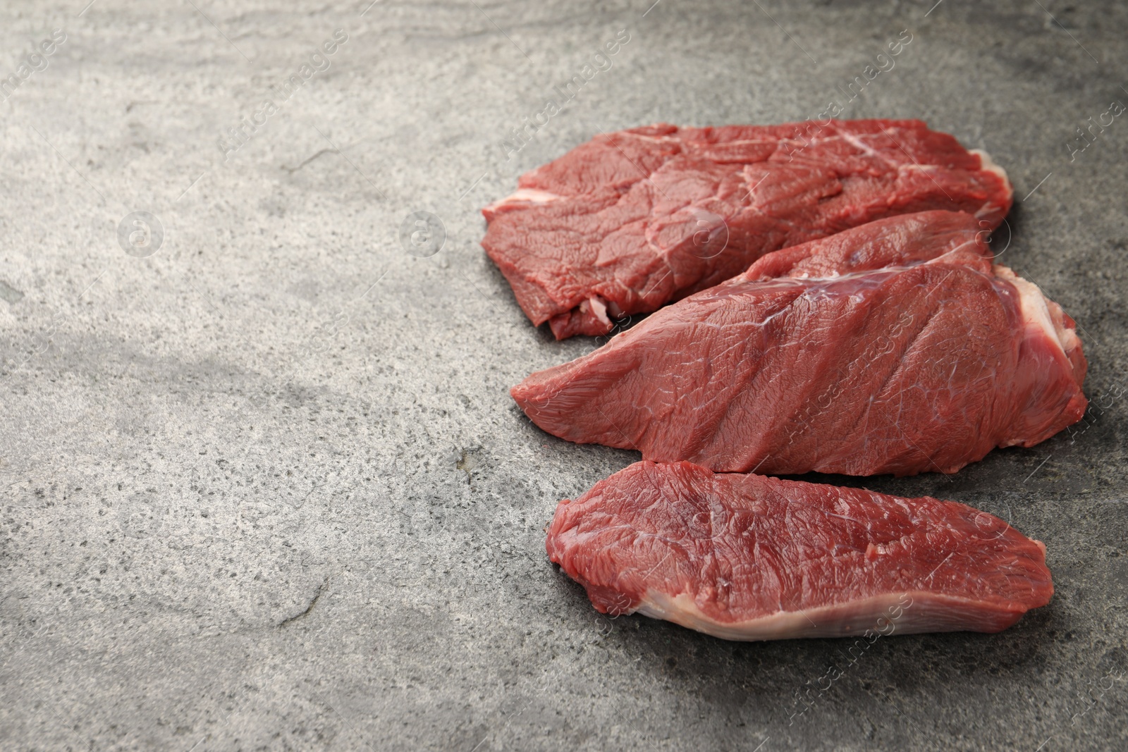 Photo of Pieces of raw beef meat on grey table, space for text