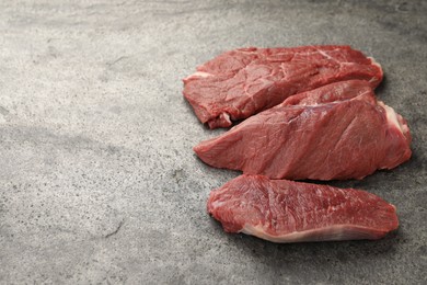 Photo of Pieces of raw beef meat on grey table, space for text