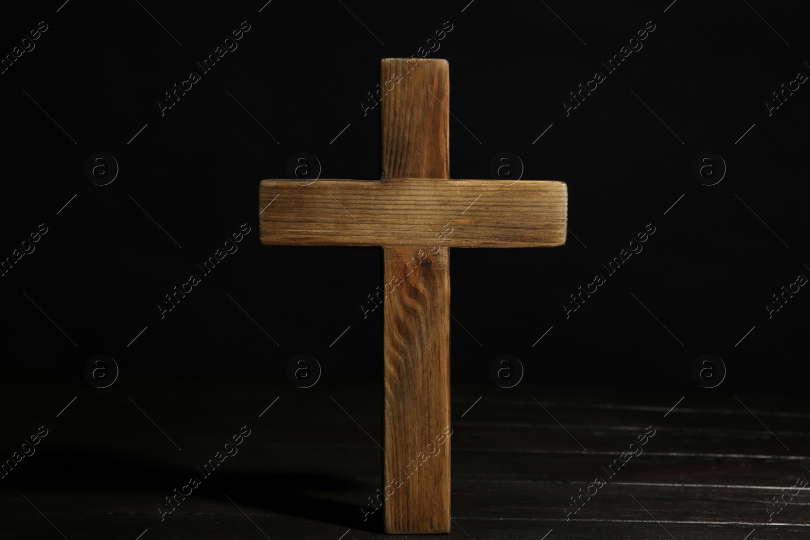 Photo of Christian cross on wooden table against black background. Religion concept