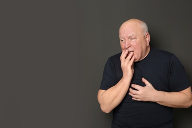 Photo of Senior man suffering from cough on dark background. Space for text