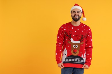 Photo of Happy young man in Christmas sweater and Santa hat on orange background. Space for text