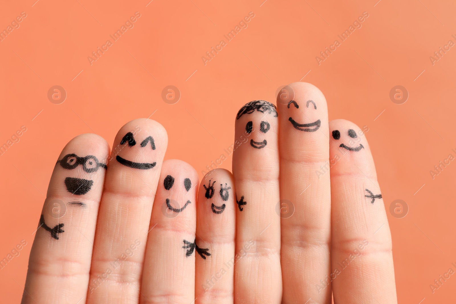Photo of Fingers with drawings of happy faces against color background. Unity concept
