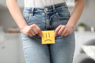 Photo of Cystitis. Woman holding sticky note with drawn sad face at home, closeup