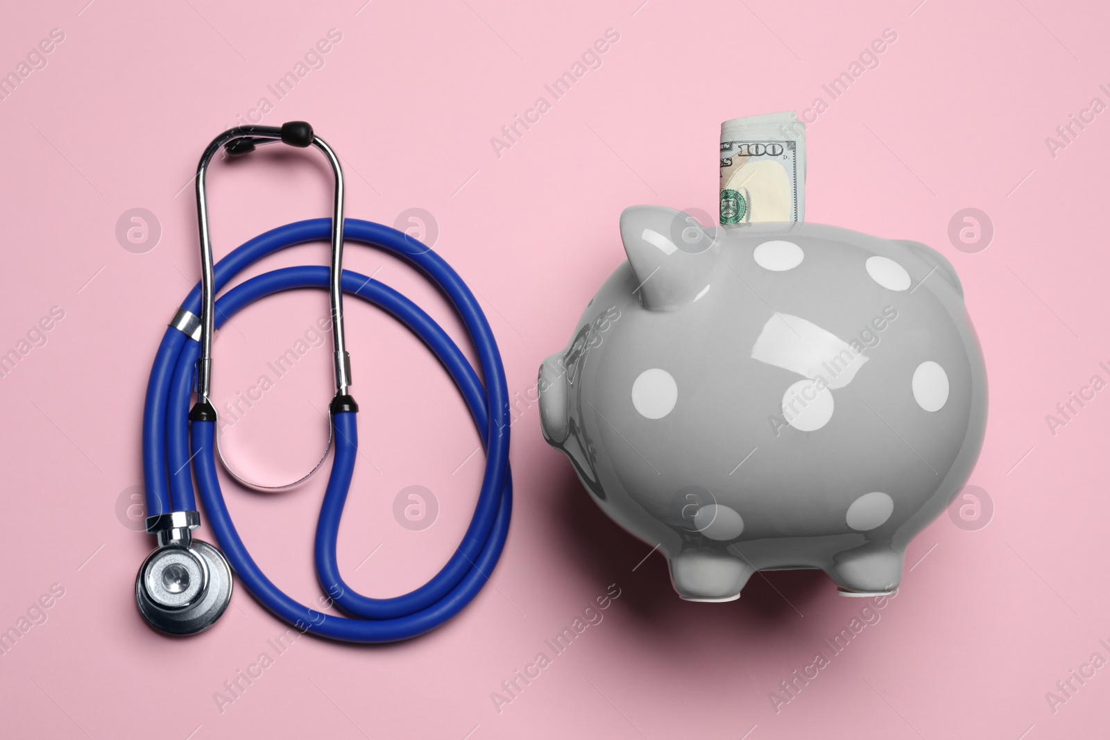 Photo of Piggy bank with money and stethoscope on pink background, flat lay. Medical insurance