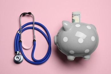 Photo of Piggy bank with money and stethoscope on pink background, flat lay. Medical insurance