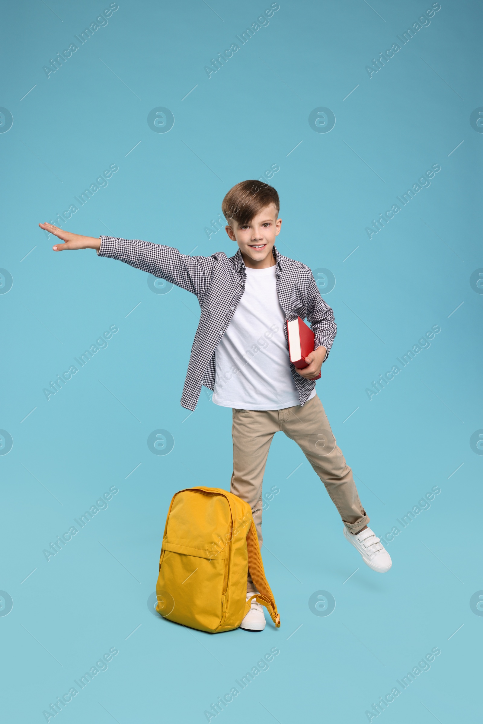 Photo of Cute schoolboy with book on light blue background