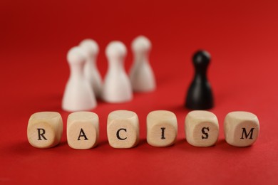 Photo of Word Racism made of wooden cubes with letters and black pawn among white ones on red background