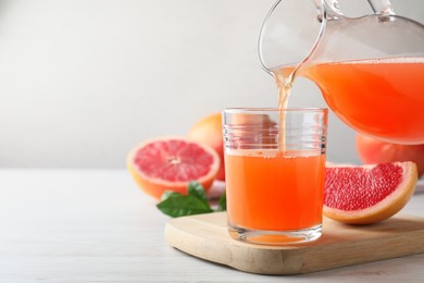 Photo of Pouring tasty freshly made grapefruit juice into glass on white wooden table. Space for text