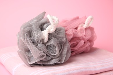 Photo of Colorful shower puffs and towel on pink background, closeup