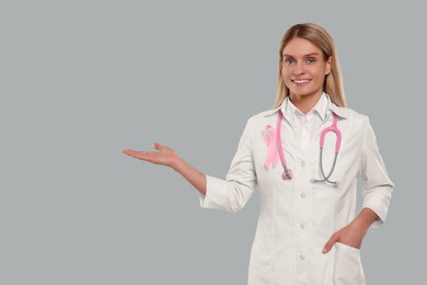 Doctor with pink ribbon and stethoscope on light grey background, space for text. Breast cancer awareness