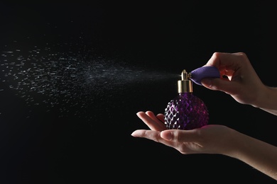 Photo of Woman holding bottle of luxury perfume on black background, closeup. Space for text