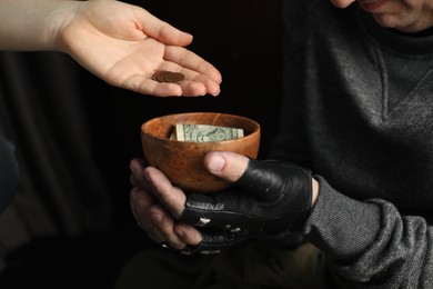 Woman giving coins to poor homeless man with bowl of donations, closeup