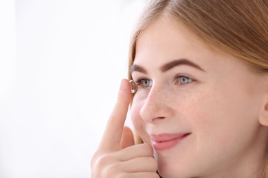 Photo of Teenage girl putting contact lens in her eye on white background