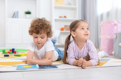 Photo of Cute little children reading book on floor in kindergarten