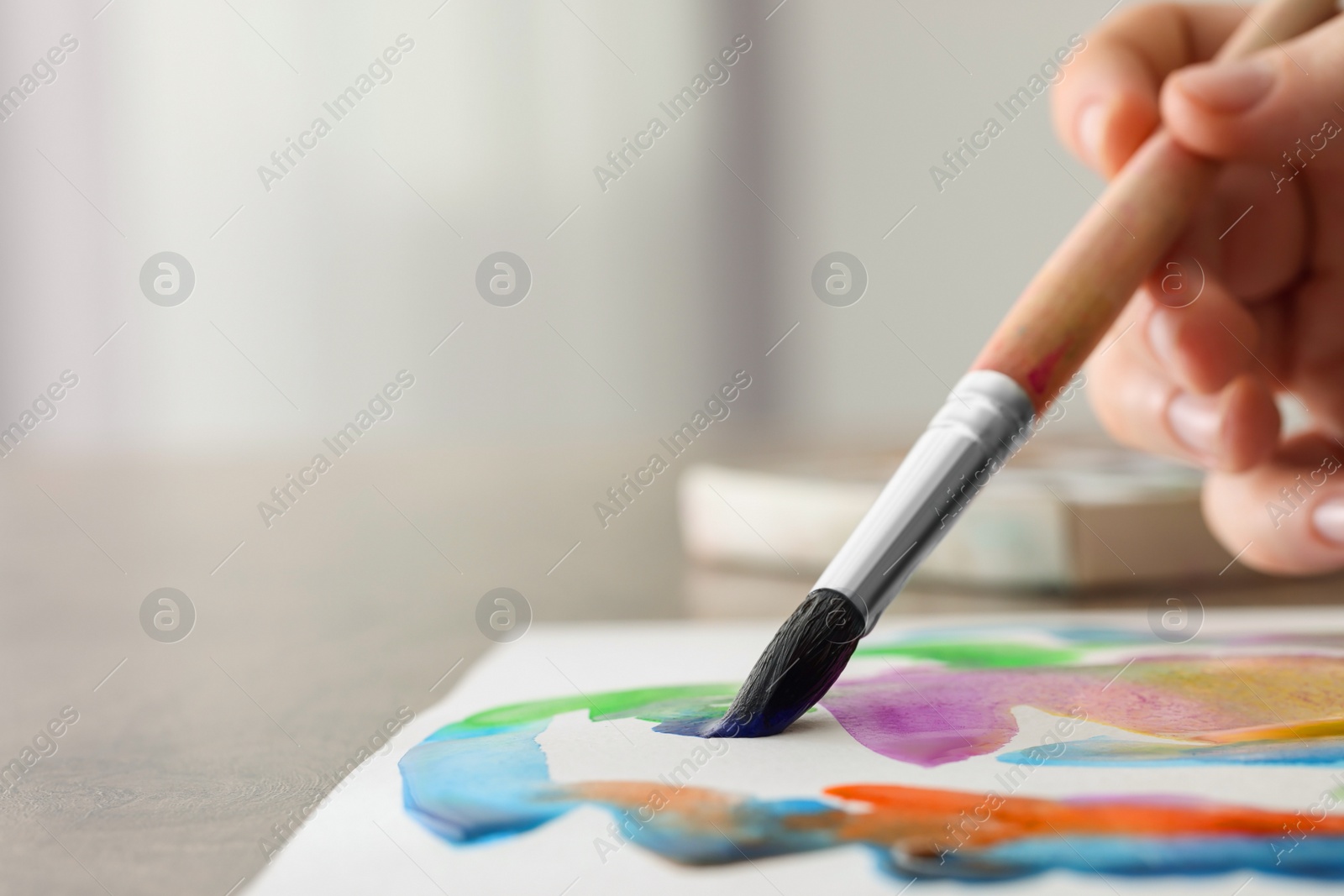 Photo of Woman painting with watercolor at wooden table, closeup. Space for text