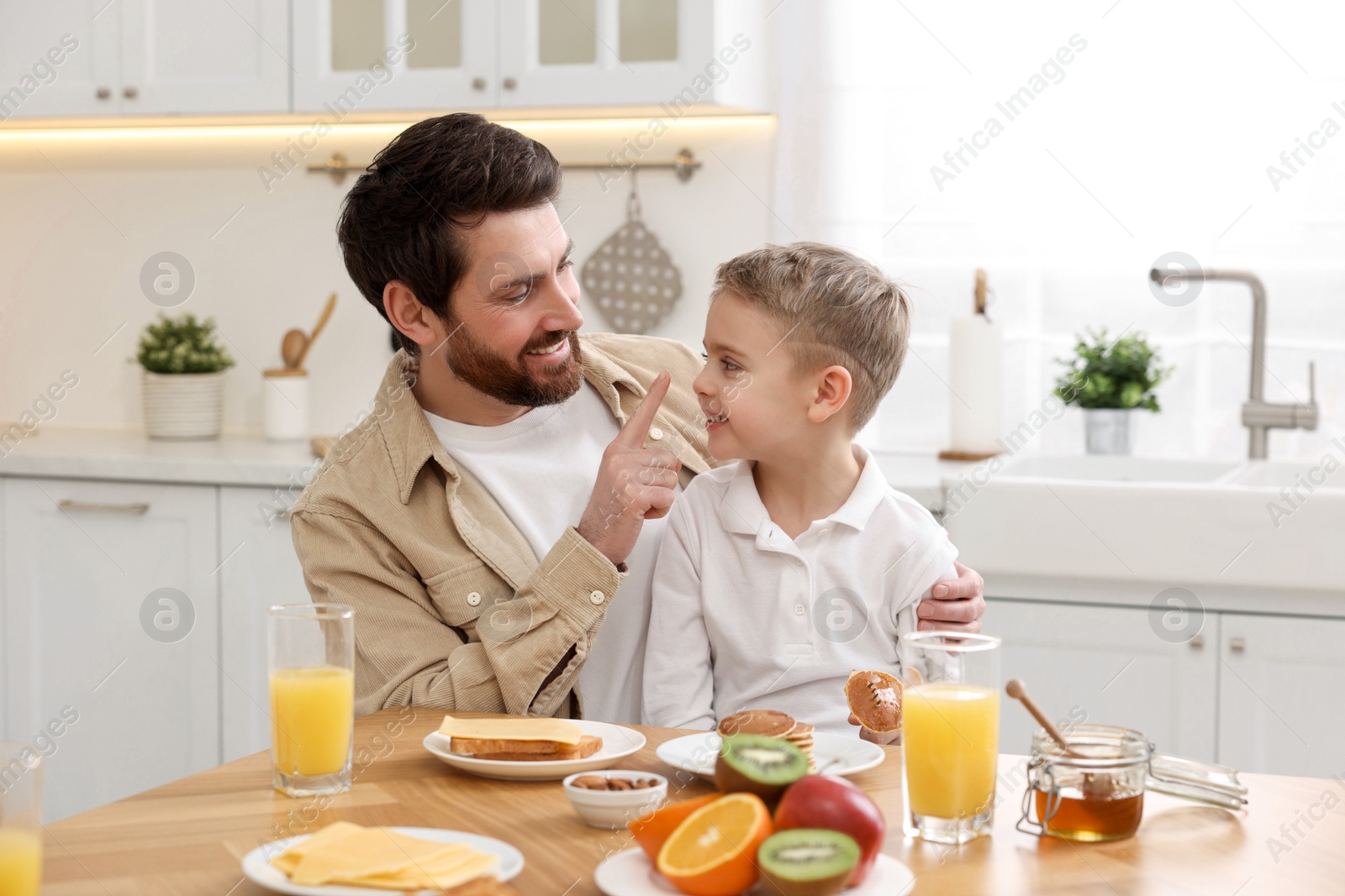 Photo of Father and his cute little son having fun during breakfast at table in kitchen