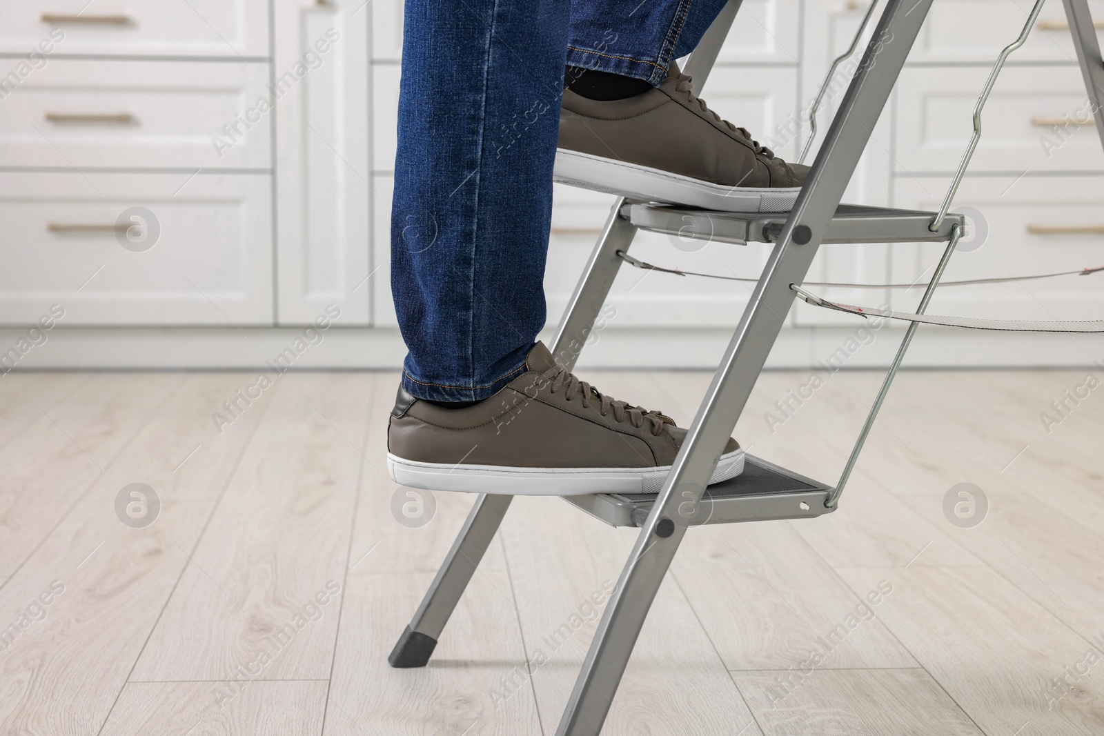 Photo of Man climbing up metal stepladder indoors, closeup