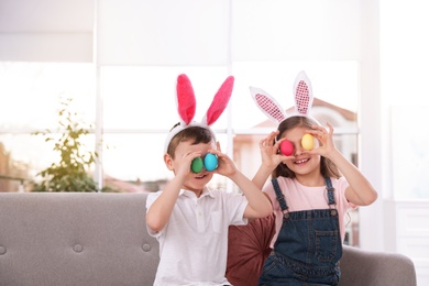 Photo of Cute little children in bunny ears headbands holding Easter eggs near eyes at home, space for text