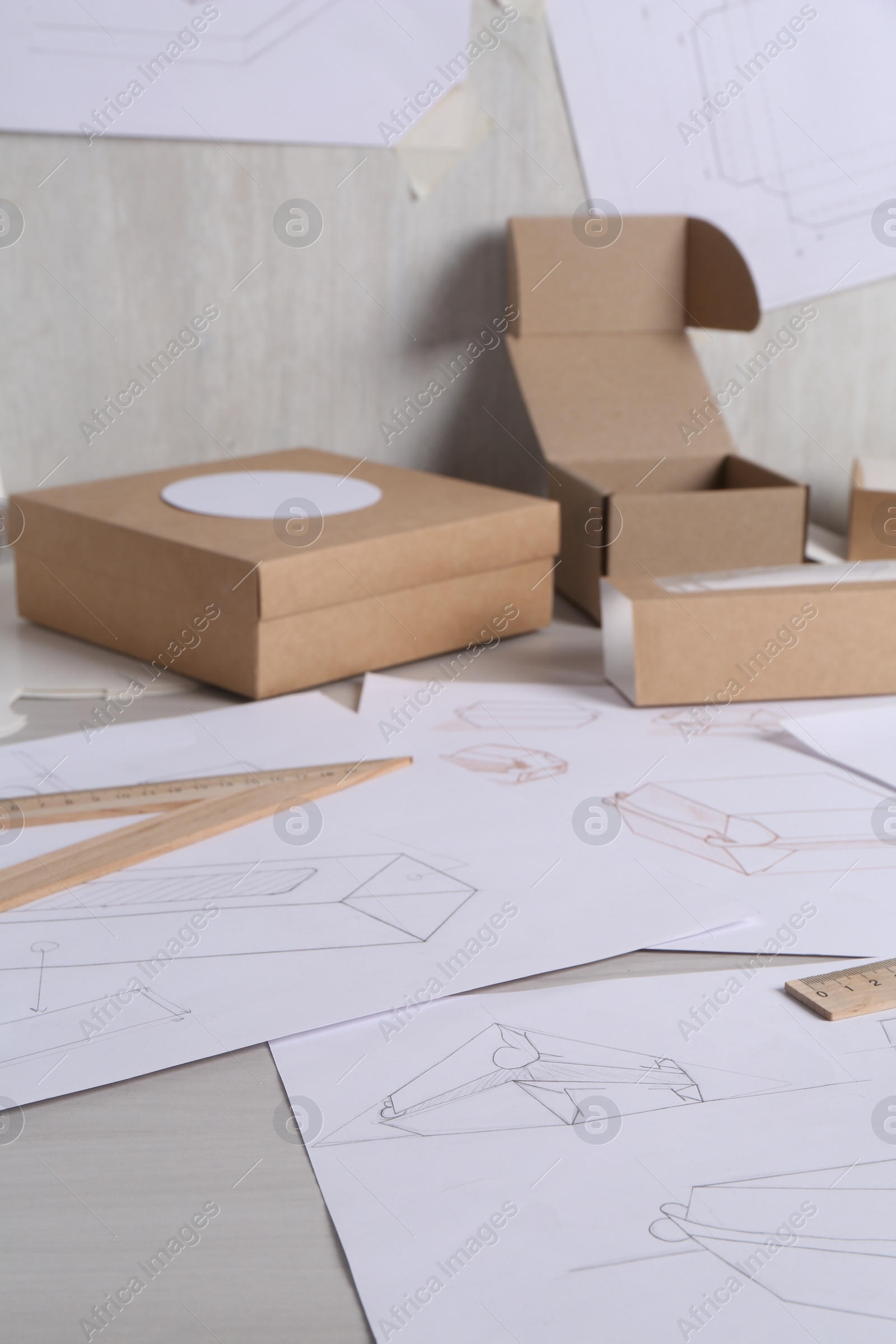 Photo of Creating packaging design. Drawings, boxes and ruler on light wooden table, closeup