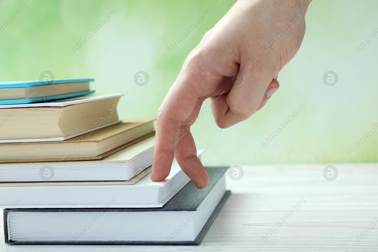 Photo of Man climbing up stairs of books with fingers on white wooden table against blurred background, closeup