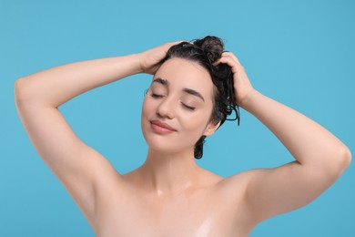 Beautiful woman washing hair on light blue background