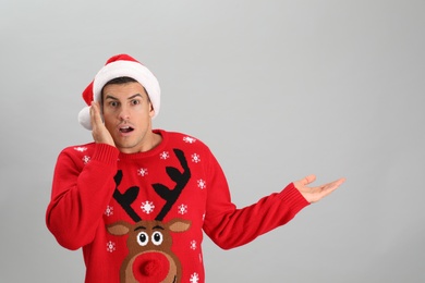 Surprised man wearing Santa hat on grey background, space for text