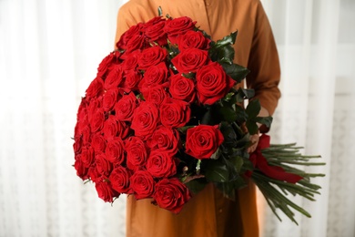 Woman holding luxury bouquet of fresh red roses indoors, closeup