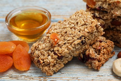 Photo of Tasty granola bars and ingredients on light blue wooden table, closeup