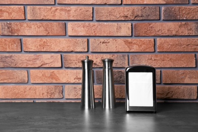 Photo of Napkin holder with salt and pepper shakers on table against brick wall. Space for text