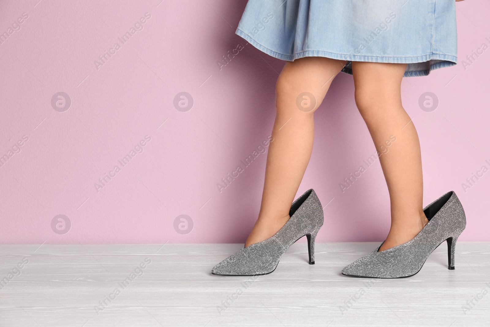 Photo of Little girl in oversized shoes near color wall with space for text, closeup on legs