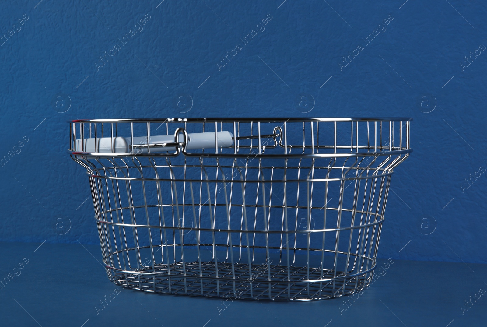 Photo of Empty metal shopping basket on blue background