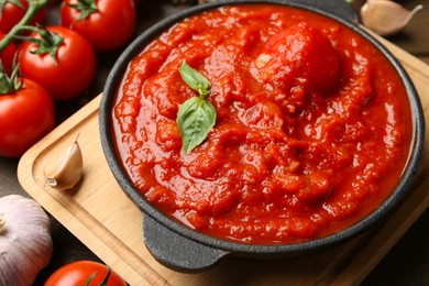 Photo of Homemade tomato sauce in bowl and ingredients on table, closeup