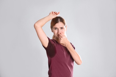 Young woman with sweat stain on her clothes against light background. Using deodorant