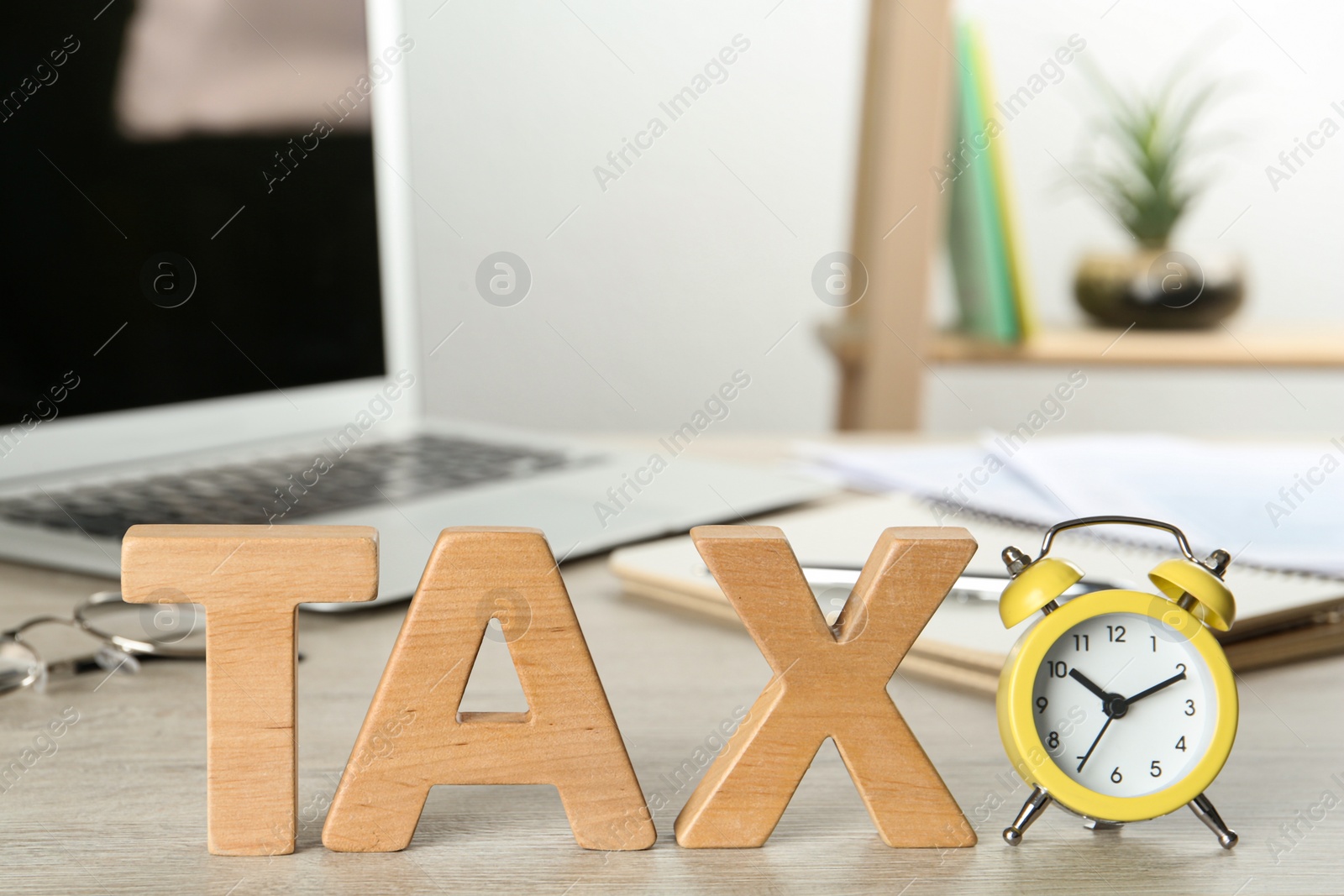 Photo of Word Tax made of wooden letters and alarm clock on white table