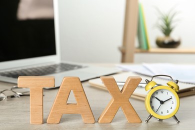 Photo of Word Tax made of wooden letters and alarm clock on white table