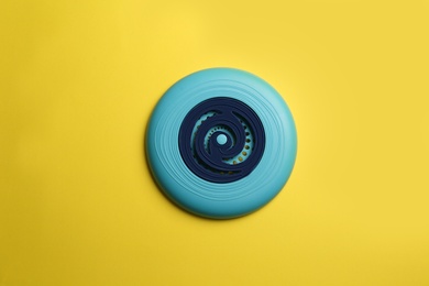 Blue plastic frisbee disk on yellow background, top view
