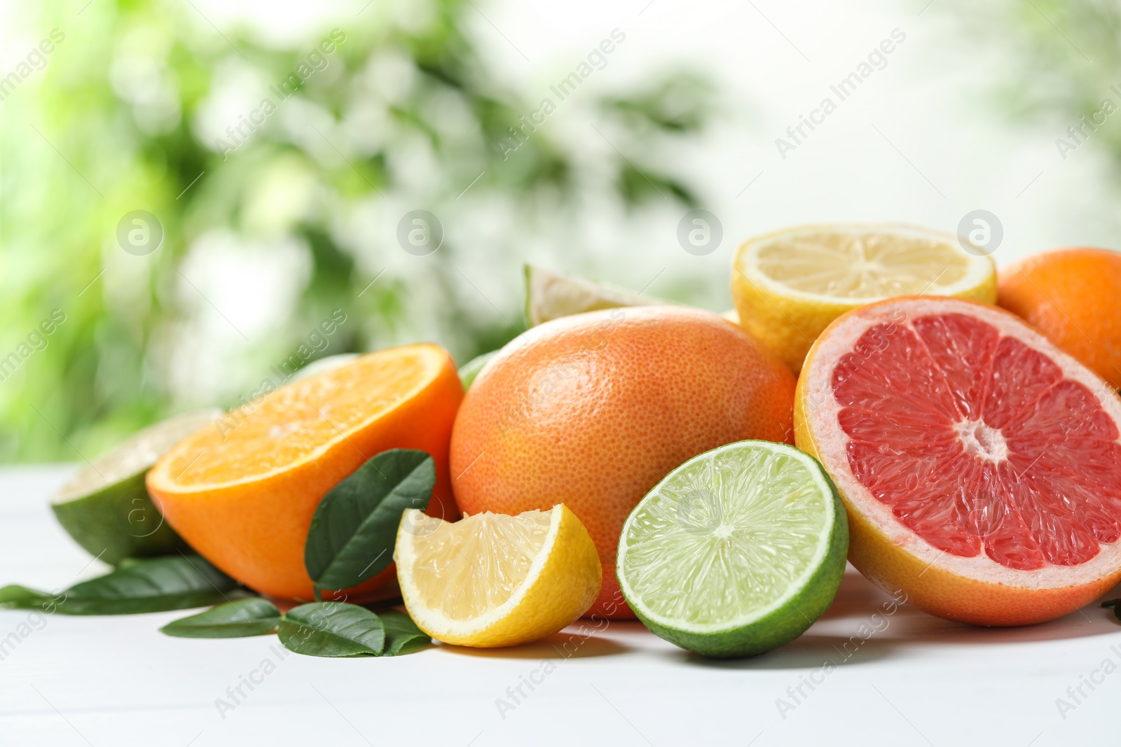 Photo of Different fresh citrus fruits and leaves on white table against blurred background, closeup