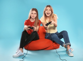 Young woman and teenage girl playing video games with controllers on color background