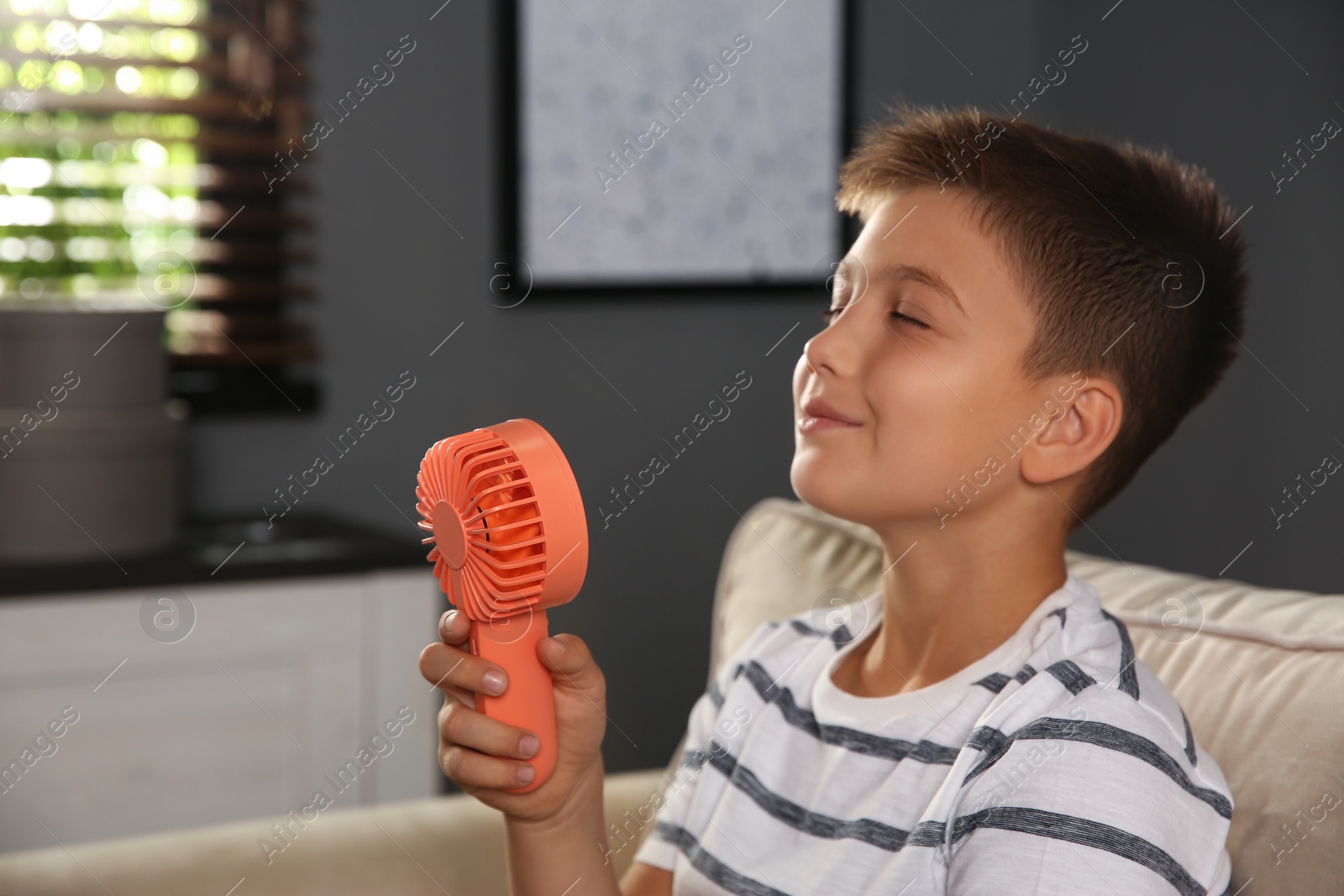 Photo of Little boy enjoying air flow from portable fan at home. Summer heat