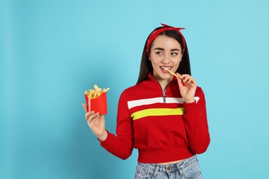 Beautiful young woman eating French fries on light blue background. Space for text