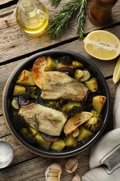 Photo of Pieces of delicious baked cod with vegetables, lemon and spices in dish on wooden table, flat lay
