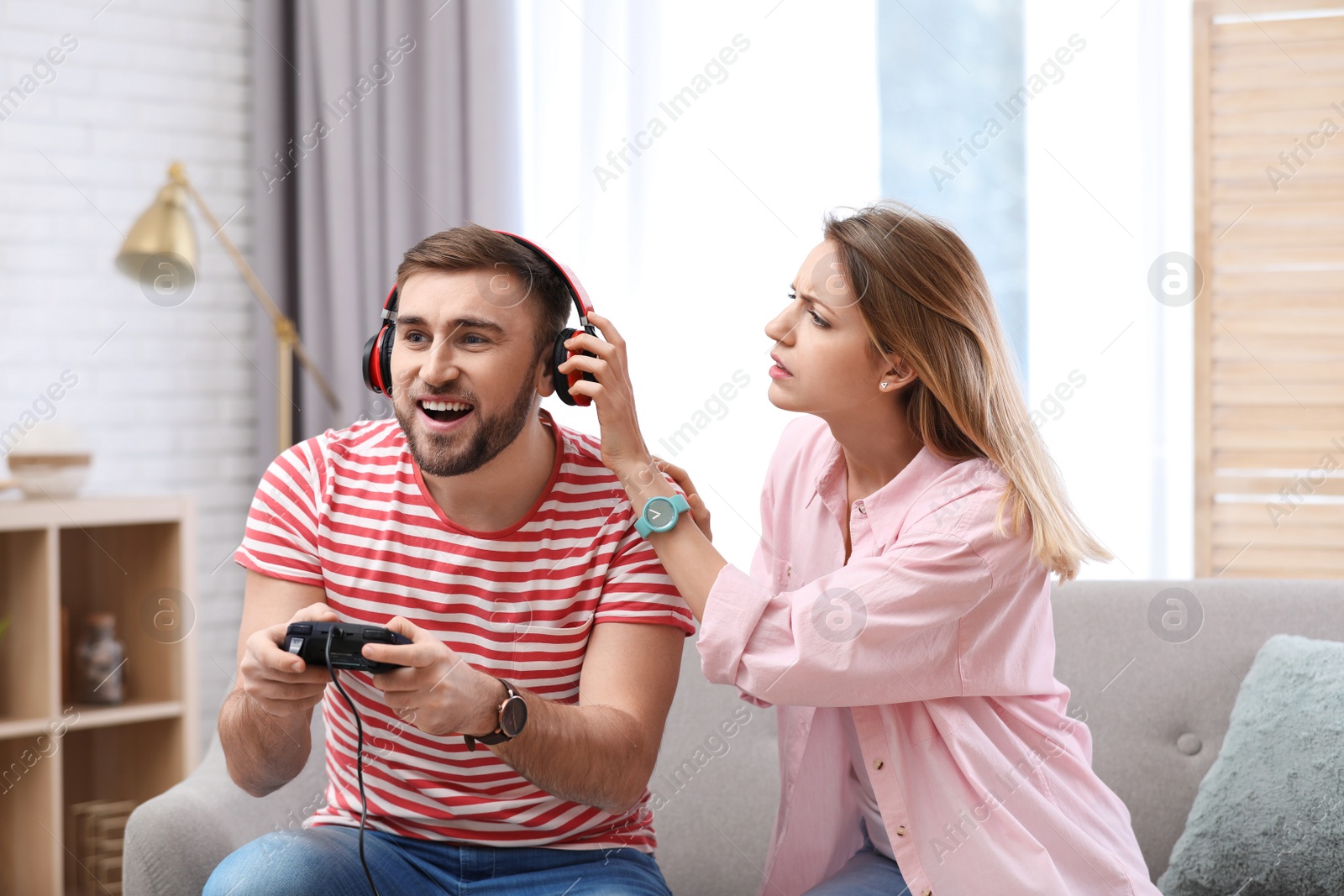 Photo of Young man playing video game at home while his girlfriend angry with him