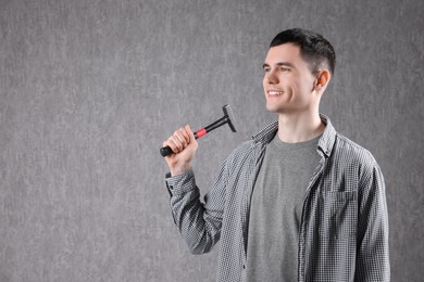 Young man holding hammer on grey background. Space for text