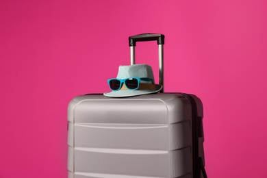 Photo of Stylish suitcase with hat and sunglasses on color background