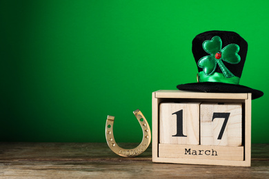 Photo of Black leprechaun hat, wooden block calendar and horseshoe on table, space for text. St. Patrick's Day celebration