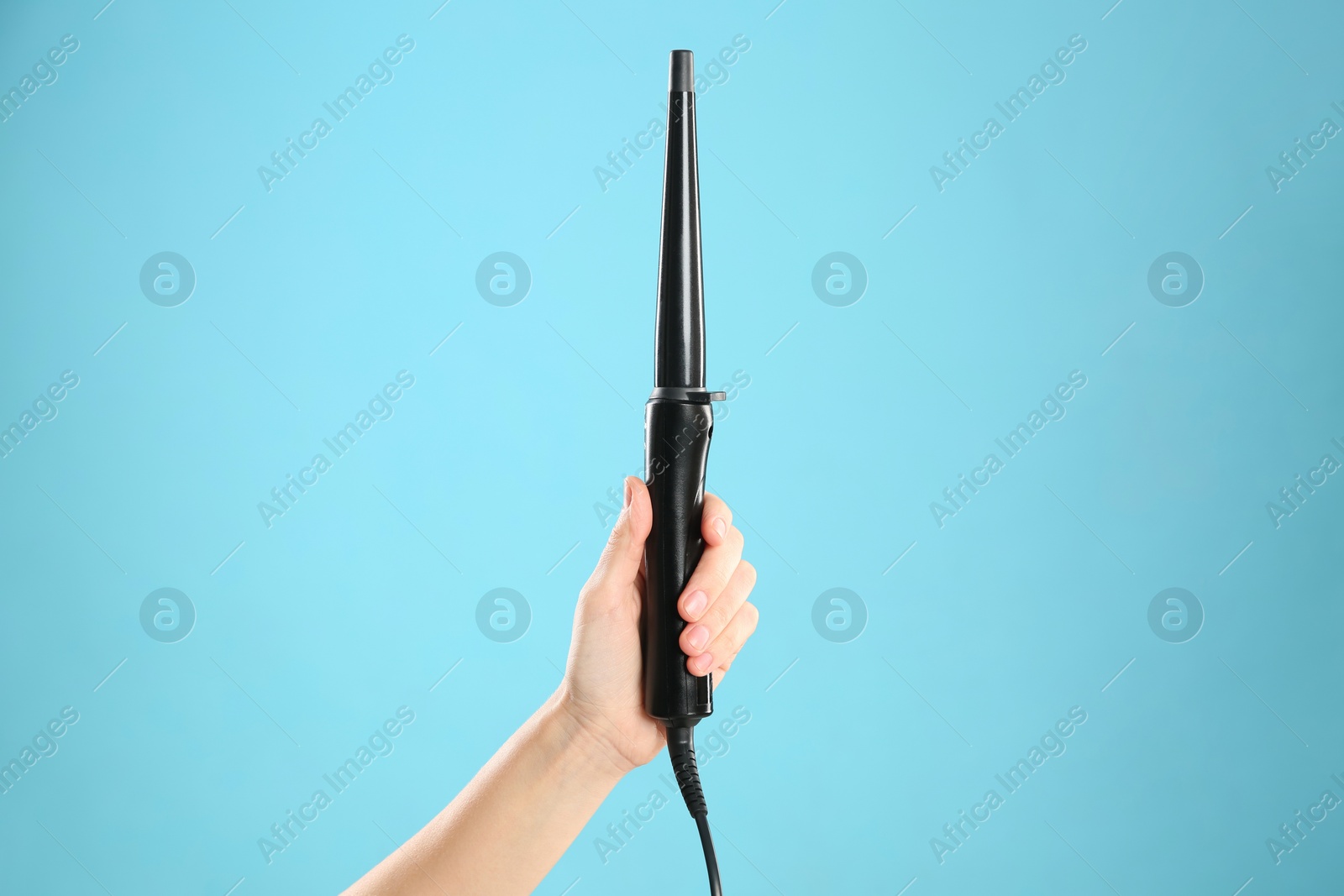 Photo of Woman holding clipless curling hair iron on light blue background, closeup