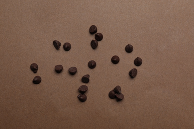 Delicious chocolate chips on brown background, top view