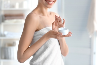 Photo of Young woman with jar of body cream at home