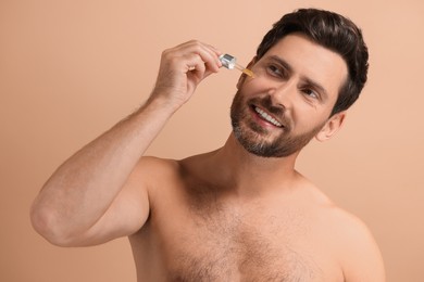Photo of Smiling man applying cosmetic serum onto his face on beige background