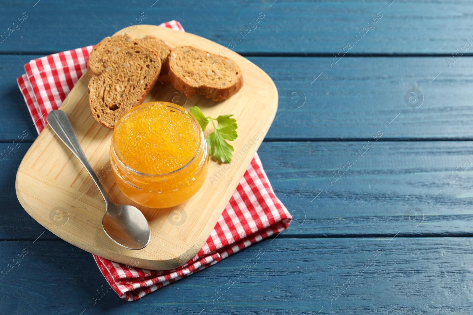 Photo of Fresh pike caviar in glass jar, bread and parsley on blue wooden table, space for text